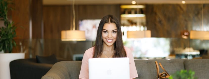 Woman smiling at camera sitting on a couch with a laptop working